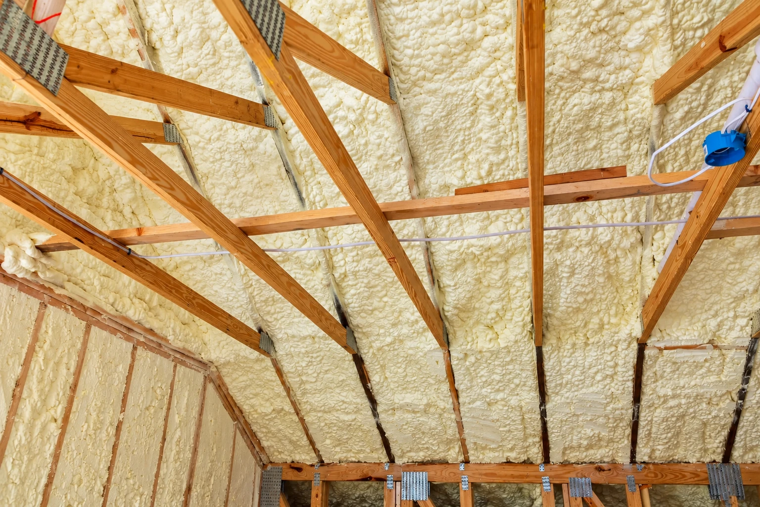 Thick cream-colored spray foam fills the roof bays between exposed wooden rafters.